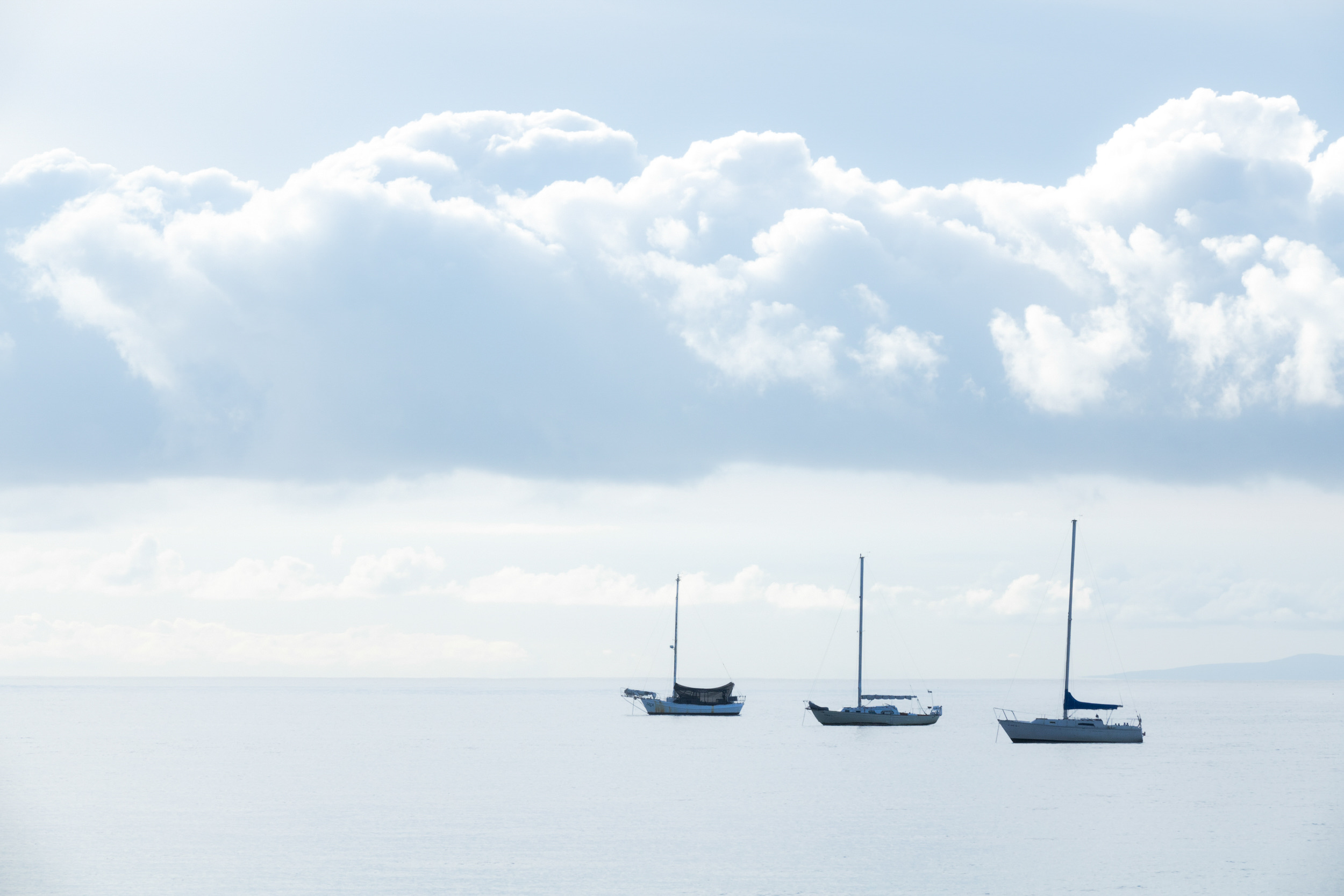Three sailboats anchored under a soft cloud bank.
